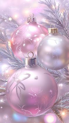 two pink and silver christmas ornaments hanging from a tree with snow flakes in the background