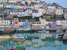 several boats are docked in the water next to some buildings and houses on top of a hill