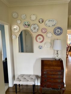 a room with plates on the wall and a dresser in front of it, along with a mirror