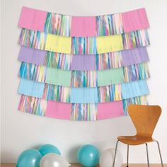 a wall hanging made out of strips of colored paper and balloons in front of it