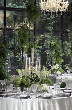 a dining room table is set with white flowers and greenery in front of a large window