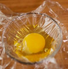 an egg yolk in a glass bowl on plastic wrapper sitting on top of a wooden table