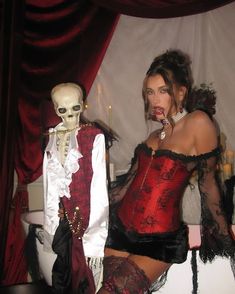 a woman in a red corset posing for the camera next to a skeleton