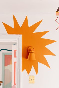 an orange light is on the wall next to a mirror and door knob with a yellow sunburst painted on it