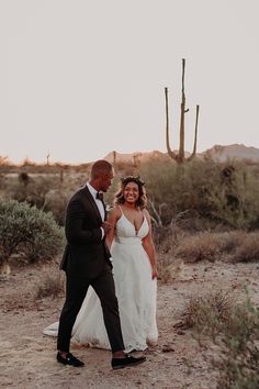 a bride and groom are walking through the desert with cacti in the background