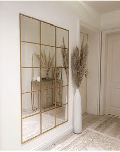 a tall white vase sitting next to a mirror on top of a wooden floor in front of a door