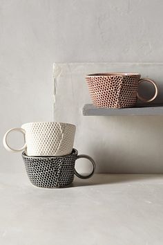 three cups sitting on top of a shelf next to each other in front of a white wall