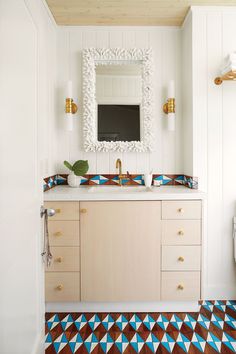 a white bathroom with blue and brown tile on the floor, sink and mirror above it