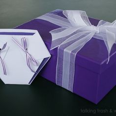 a purple gift box with a white bow and ribbon on it sitting next to a card