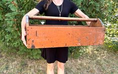 a woman standing in front of a bush holding a large wooden box over her head