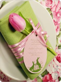 a pink tulip sitting on top of a plate next to a green napkin with a tag