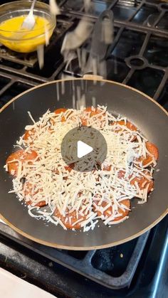 a skillet with cheese and hotdogs cooking on top of an open stove