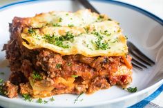 a white plate topped with lasagna covered in meat and cheese next to a fork