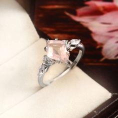 a pink diamond ring sitting on top of a wooden table next to a white flower