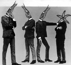 four men in suits and hats with their hands on each other's heads, all wearing fish masks