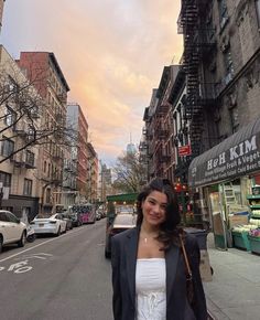 a woman standing on the side of a street next to tall buildings and parked cars