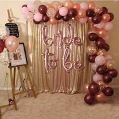 a balloon arch with the word bride to be spelled in pink, gold and burgundy balloons