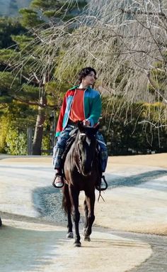 a man riding on the back of a brown horse next to a park filled with trees