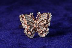 a butterfly shaped diamond ring sitting on top of a blue velvet covered surface with its wings spread