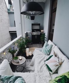 an outdoor living area with white and green pillows on the couches, potted plants and a grill in the background