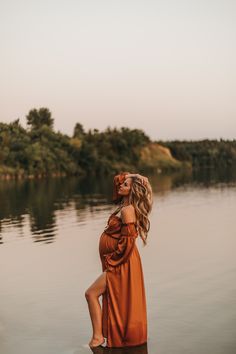 a woman in an orange dress sitting on the edge of a body of water