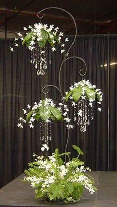 an arrangement of white flowers and greenery on a table in front of a black curtain