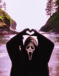 a person making a heart shape with their hands while standing in front of a river