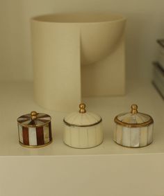 three small containers sitting on top of a counter next to a white vase and stack of books