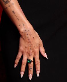 a woman's hand with tattoos and a ring on her left wrist, holding onto an emerald stone