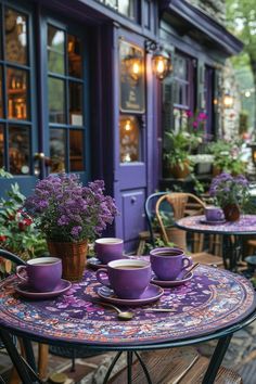 purple coffee cups and saucers sit on an outdoor table in front of a cafe