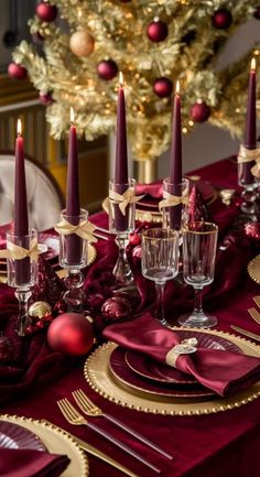 a table set for christmas with red and gold plates, silverware and candlesticks