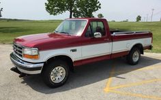 a red and white pick up truck parked in a parking lot next to a tree