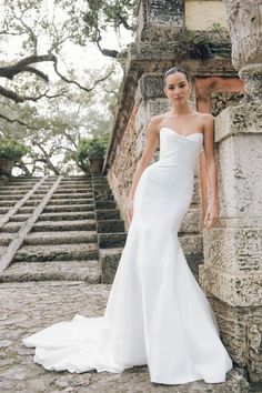 a woman standing in front of some stairs wearing a white wedding dress with one shoulder