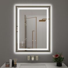 a bathroom sink sitting under a large mirror with lights on it's sides and a plant next to it