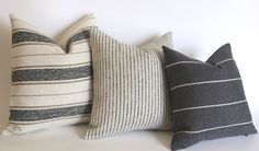 three pillows are lined up on a white surface, one is black and the other is gray