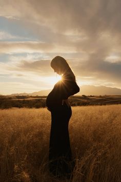 a pregnant woman standing in a field at sunset