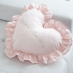 a pink heart shaped pillow sitting on top of a white couch with the word love you written on it