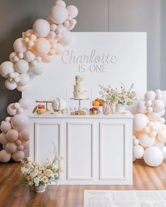 a table with balloons and cake on it in front of a sign that says charlotte is one