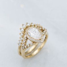 a gold ring with a pear shaped diamond surrounded by small white pearls on the sides