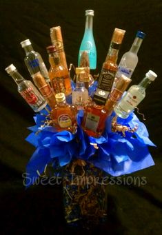 a vase filled with liquor bottles on top of a black tablecloth covered floor next to a blue ribbon