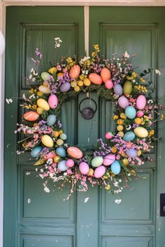 a green door with a wreath decorated with easter eggs and flowers on the front porch