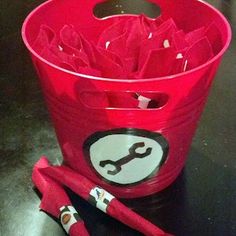 a red bucket filled with scissors on top of a black table next to two markers