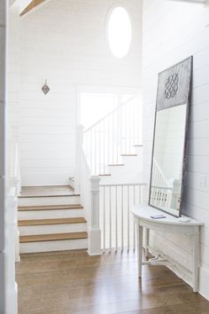 a mirror sitting on top of a wooden floor next to a stair case in a white house