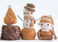 three crocheted snowmen sitting next to each other on top of balls of yarn