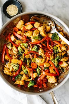 a pan filled with chicken, broccoli and red peppers on top of a table