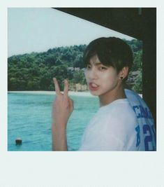 a young man making the peace sign with his hand while standing in front of water