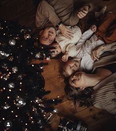 three people laying on the floor next to a christmas tree