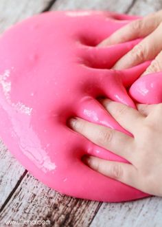 a child's hand touching a pink doughnut on top of a wooden table