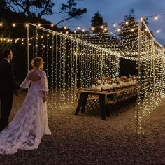 a bride and groom standing in front of a table covered with fairy lights