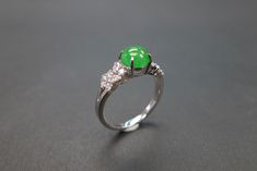 an emerald and diamond ring sitting on top of a gray surface with white diamonds around it